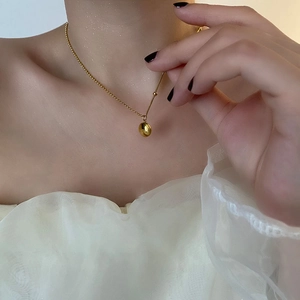 Minimalist gold titanium bean pendant necklace on female model with warm lighting
