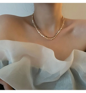 Close-up of double-layer gold necklace with colorful beads and white pearls on woman's collarbone