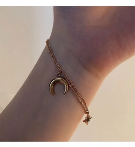 Détail de pendentifs lune et étoile dorés sur une chaîne double en acier titane