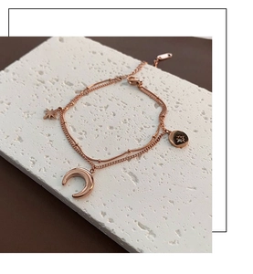 Détail de la chevillère double couche étoile et lune en or rose sur une surface en pierre