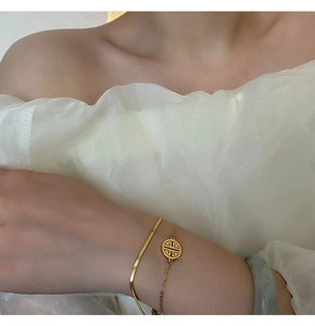 Close-up of gold layered ankle bracelets with hollow Fu pendant and green jade bangle