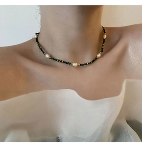 Detail of beaded necklace featuring green faceted stones and elegant white pearls