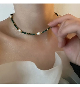 Detail of turquoise and pearl choker necklace on neck, featuring faceted green stone beads