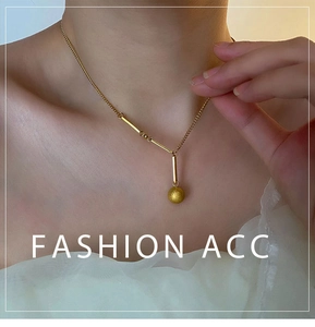 Détail du pendentif perle mate dorée et barre sur une chaîne en acier inoxydable