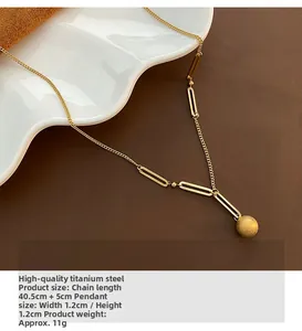 Gros plan du pendentif boule dorée mate sur chaîne en acier titane avec décor céramique