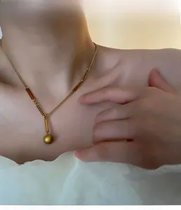Vue détaillée du pendentif boule dorée mate et de la chaîne en acier titane sur mannequin