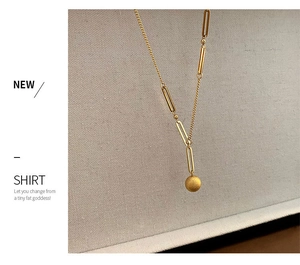 Détail du pendentif sphère dorée mate avec chaîne asymétrique en acier inoxydable