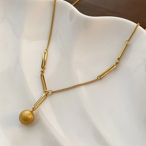 Collier élégant en titane doré avec pendentif boule mate sur un plateau en céramique