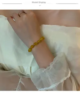 Gros plan d'un bracelet en perles de pierre jaune avec détails dorés portés sur dentelle