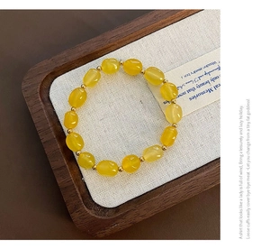Détail d'un bracelet en pierre naturelle jaune avec perles dorées sur plateau bois