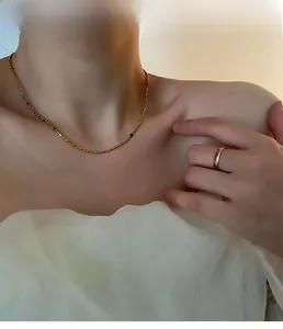 Detail of gold chain necklace with colorful beads and minimalist ring on model