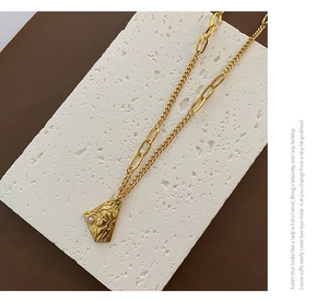 Macro detail of a gold titanium necklace with a relief triangle pendant and pearl