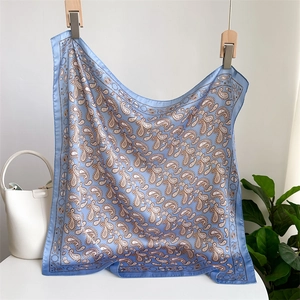 Blue paisley silk scarf displayed on wooden hangers with a stylish white handbag