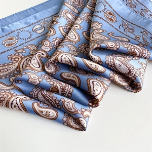 Detailed macro view of paisley pattern on light blue satin scarf with hand-rolled edges