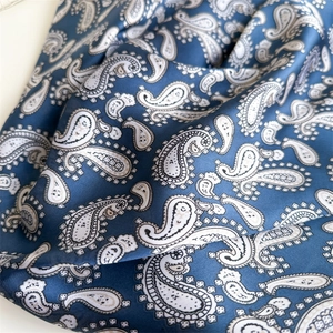 Detailed close-up of navy blue paisley silk scarf with intricate white and black patterns