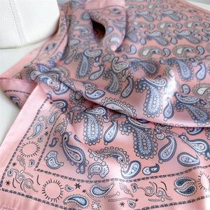 Detail of pink silk scarf featuring blue paisley and celestial patterns with a glossy finish