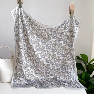 Detail of white paisley silk scarf with butterfly pattern hanging next to a bucket bag