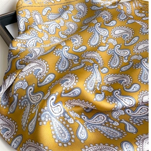 Close-up of a mustard yellow silk scarf featuring detailed blue paisley patterns