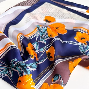 Satin silk scarf featuring navy blue and orange floral geometric patterns in folded view