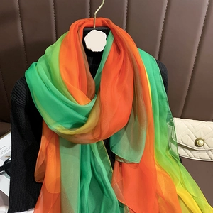 Détail d'un châle en mousseline dégradé vert émeraude et orange vif sur un cintre