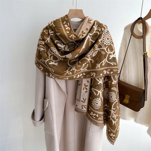 Close-up of brown floral cashmere-feel scarf with elegant fringes draped over a wool coat