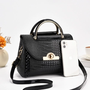Détail du sac à main noir verni effet crocodile avec fermoir doré et un smartphone