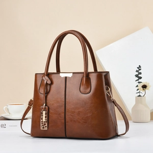 Detail of dark brown leather tote bag with gold hardware and elegant metal pendant charm