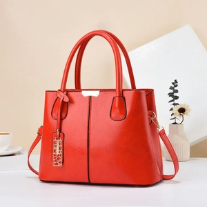 Close-up of vibrant red leather tote bag with round metal charm and detachable shoulder strap
