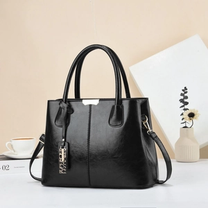 Close-up of black polished leather handbag with gold metal plaque and charms