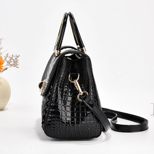 Détail d'un sac à main noir à texture crocodile avec poignée en métal doré