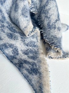 Close-up of thick blue and cream boucle yarn scarf with soft frayed tassel edges
