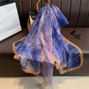 Elegant lightweight blue silk shawl draped on a leather bag with stylish sunglasses