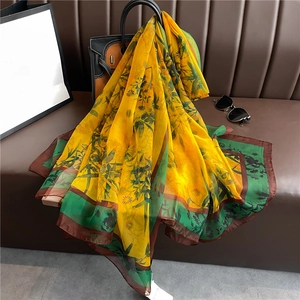 Elegant yellow silk scarf with green bamboo prints and brown borders on leather sofa