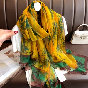 Long silk scarf with tropical flower print in yellow and green draped on a white shirt