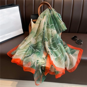 Detail of green leaf pattern silk scarf with orange edge draped over a brown handbag