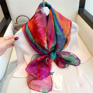 Large silk-feel scarf with colorful feather print styled on a white sweater