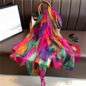Elegant large silk scarf with abstract colorful print draped on a leather handbag