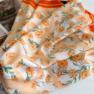 Detailed close-up of orange floral silk scarf with elegant satin twill texture