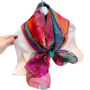 Large silk-feel scarf with colorful feather print draped over a white knitted sweater