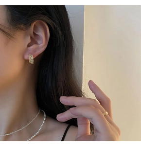 Détail de créoles dorées en C texturées avec cœur en zircon portées par un mannequin