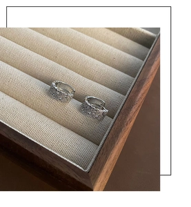 Détail de boucles d'oreilles huggie argentées serties de zircons sur fond de lin