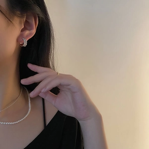 Boucles d'oreilles créoles en argent S925 avec zircons portées sur fond beige