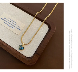 Detailed view of a golden heart pendant with iridescent abalone shell inlay on a wooden tray