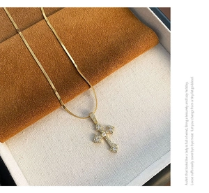 Détail d'un pendentif croix doré serti de zircons sur une chaîne de type serpent