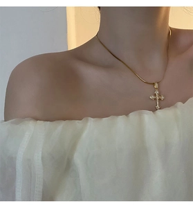 Gros plan du pendentif croix dorée avec zircons porté sur un chemisier blanc