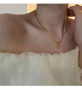 Close-up of a gold heart pendant with 3D rose detail on a flat snake chain worn by a model
