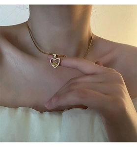 Close-up of golden heart pendant with a rose and crystals on a fine snake chain necklace