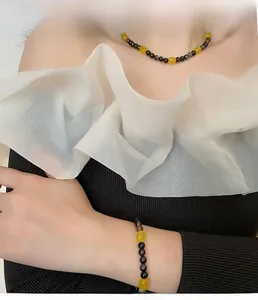 Detail view of yellow beaded necklace and bracelet set worn by a model in black outfit