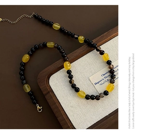 Detail of yellow amber-style beads and black beads with golden lobster clasp and chain