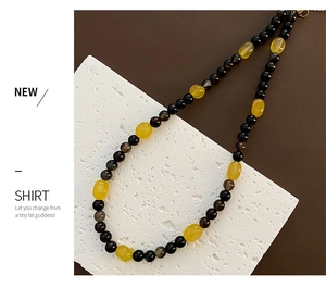 Detail of beaded necklace with yellow stone pendant and black beads on stone surface